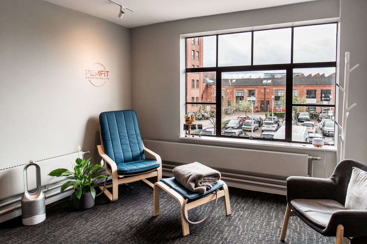 Modern PEMF Therapy area with a blue PEMF chair, gray armchair, and large window.